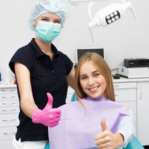 Female hygienist and patient holding their thumbs up